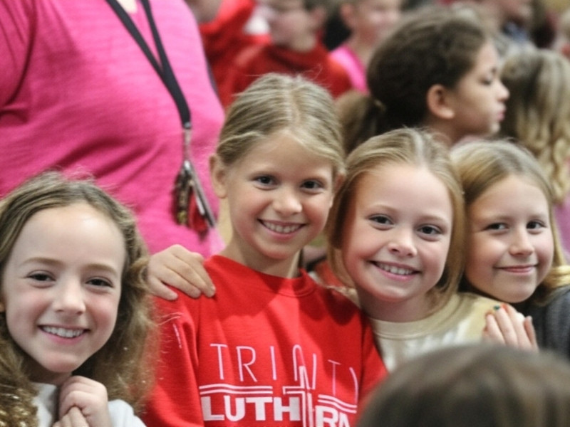 Four elementary girls embracing each other smiling at the camera.